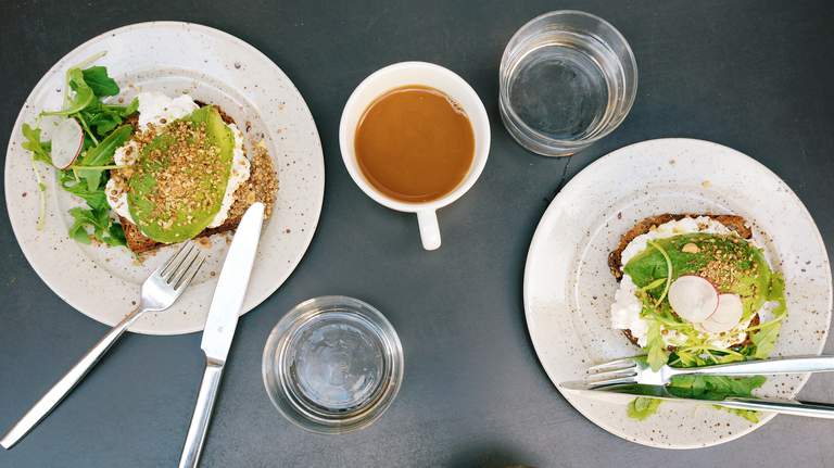 Breakfast in Stockholm. A table is set wit two avocado sandwiches, a cup of coffee and glasses of water.