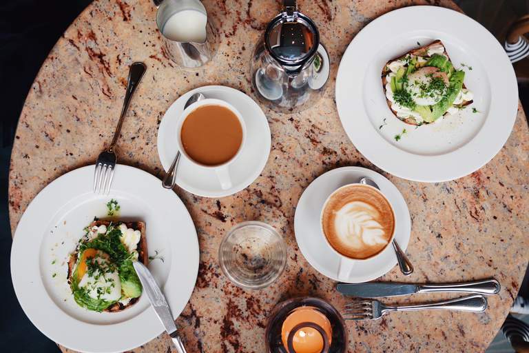 Two avocado sandwiches with poached eggs on top and two cups of coffee on a pink marble table