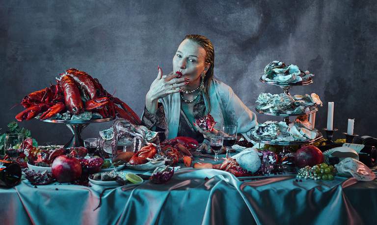 A person sitting at the table covered with seafood, fruit and wine.