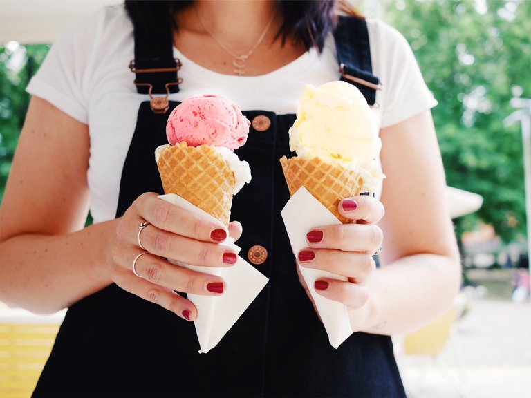A person with a black dress is standing outside holding two ice cream cones