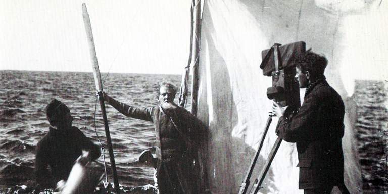 1917: Bakom kulisserna fotografi från inspelningen av den svenska stumfilmsklassikern Terje Vigen. Den legendariska regissören och skådespelaren Victor Sjöström står i mitten, omgiven av sitt lilla filmteam. I bakgrunden syns havet i Stockholms skärgård.