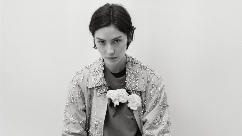 A person is wearing an ornate, beaded jacket and holding a small bouquet of flowers.