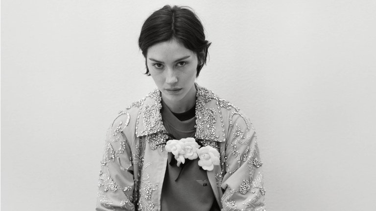 A person is wearing an ornate, beaded jacket and holding a small bouquet of flowers.