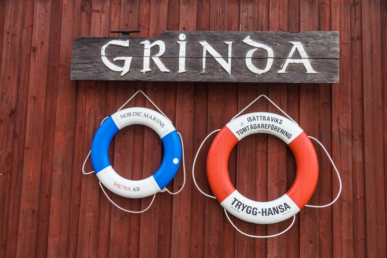 A sign with the name of the island Grinda and two lifebuoys on a wall.