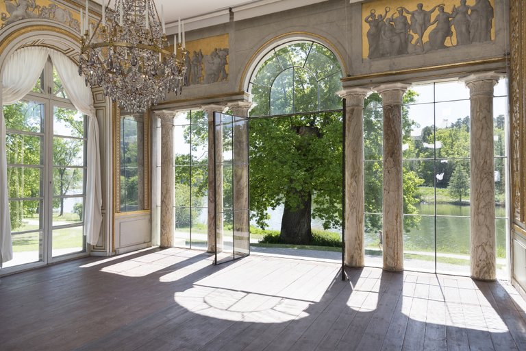 A part of the pavilion adorned with crystal chandeliers and columns, opening up to a beautiful view of lush green trees.