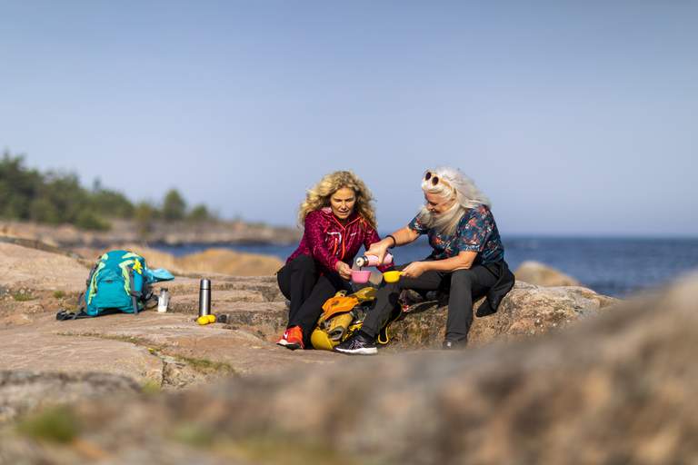 Hiking trails in Stockholm. Two women, dressed in hiking gear with comfortable shoes and backpacks, are taking a coffeebreak during a hike in the archipelago.