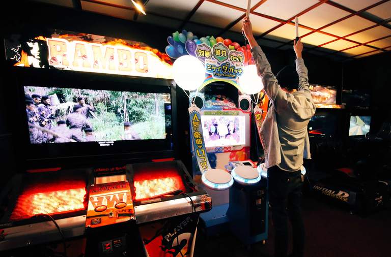 Activities in Stockholm. A man stands with both arms over his head, playing and arcade game at Hey STHLM!.