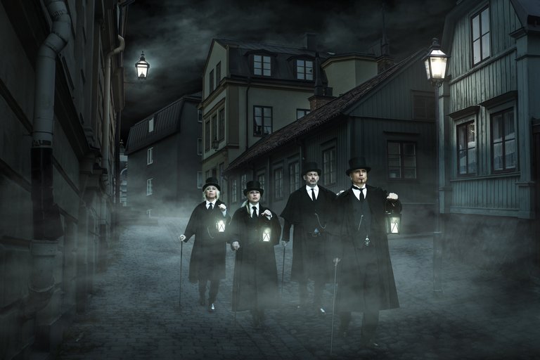 Four people in black coats and lanterns in their hands are walking in the Old Town at night