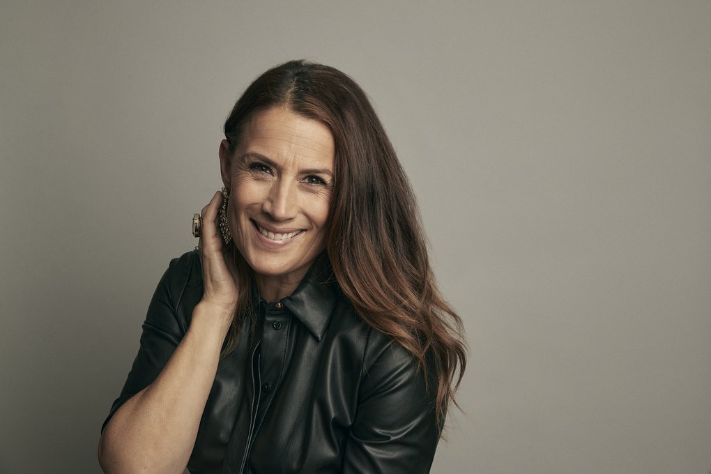A smiling woman with semi-long, brown hair and a black leather jacket.