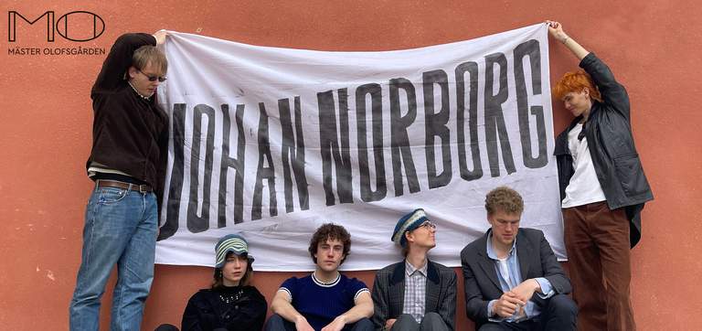 Two people holding a banner with the name Johan Norborg on it. Four other people sitting under the banner.
