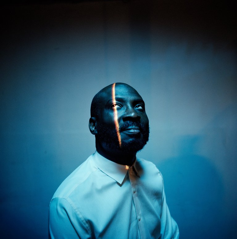 A man in a white shirt looks up at a light shining down on his face.