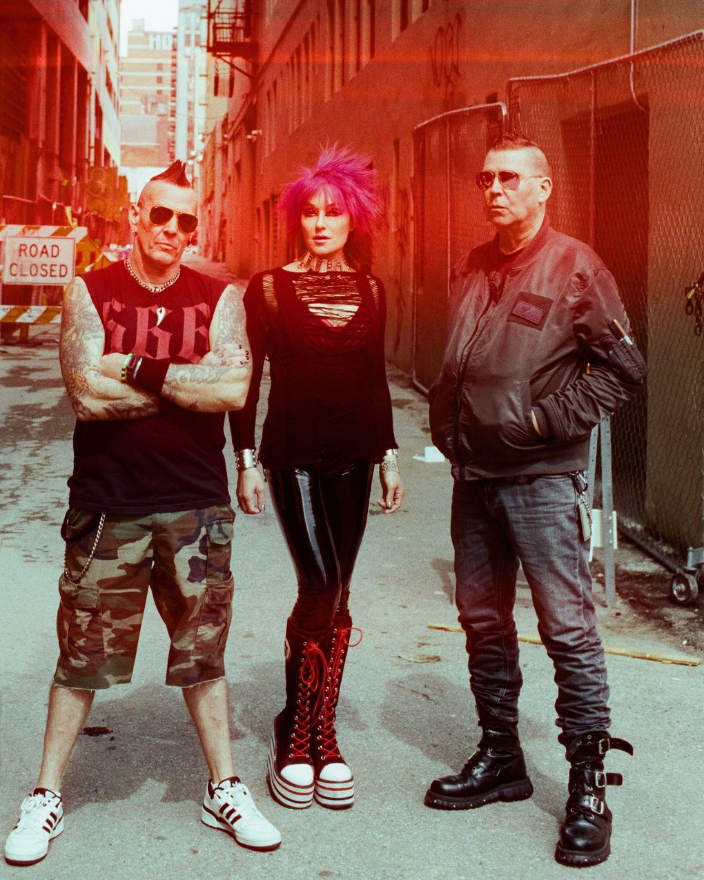 The members of KMFDM standing in a dilapidated alleyway.