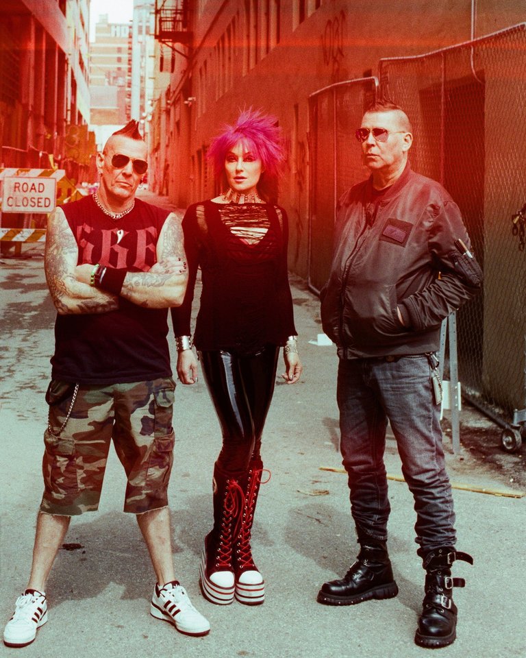 The members of KMFDM standing in a dilapidated alleyway.