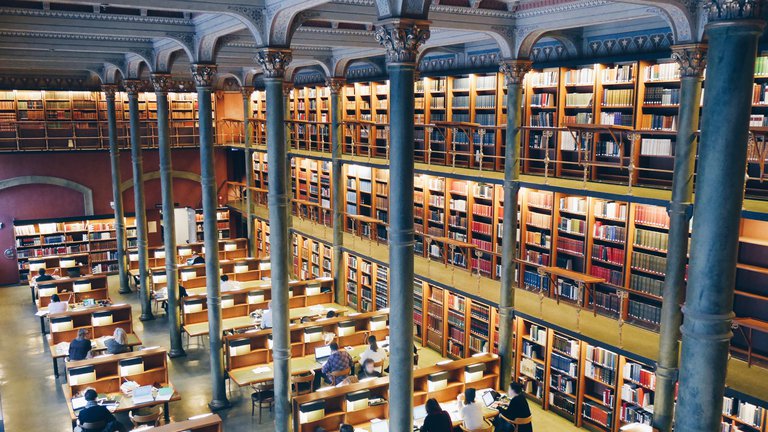 Attractions in Stockholm. The Royal Library. People are sitting along long tables in the library's main reading room.
