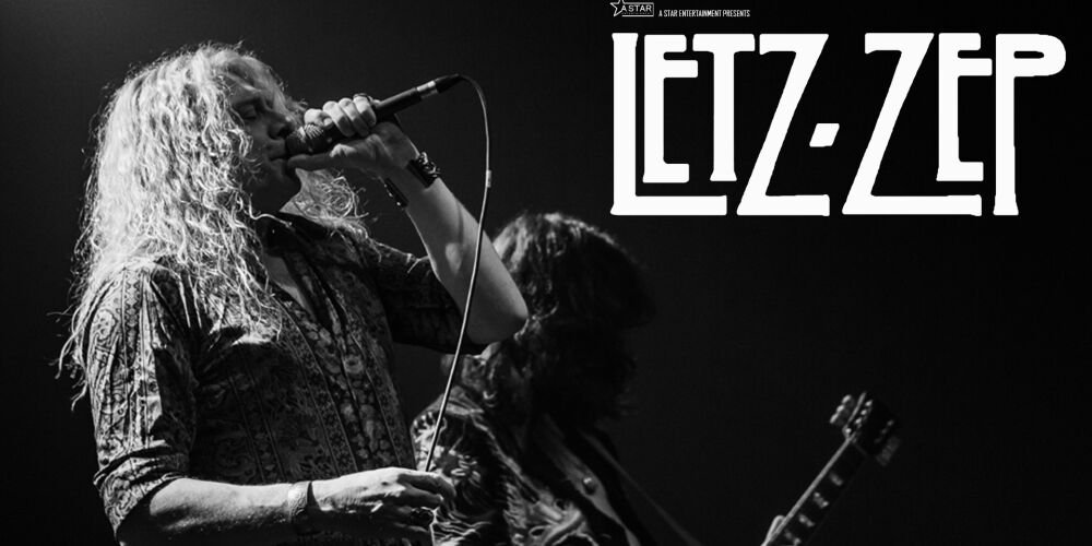 A black-and-white concert image shows a singer with long curly hair singing into a microphone on stage. A guitarist appears in the background, and the text “LEZZ ZEP” is displayed prominently beside them. The image conveys energy, a rock atmosphere, and a live performance.