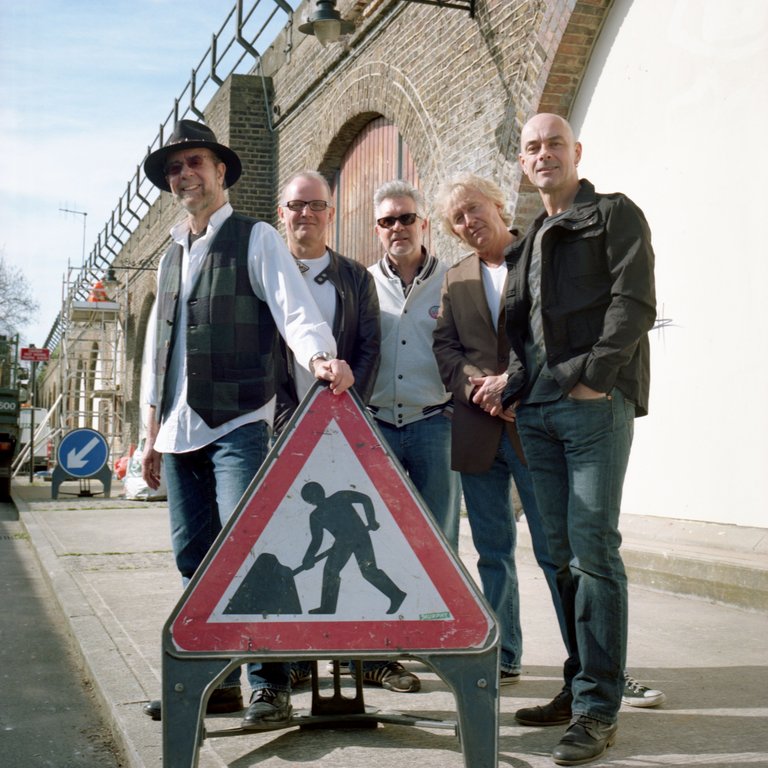 Five men by roadworks sign, brick viaduct.