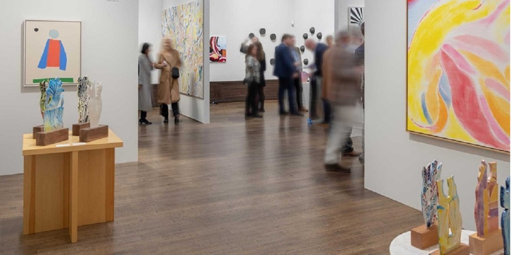 Exhibition hall with paintings, sculptures, and visitors.