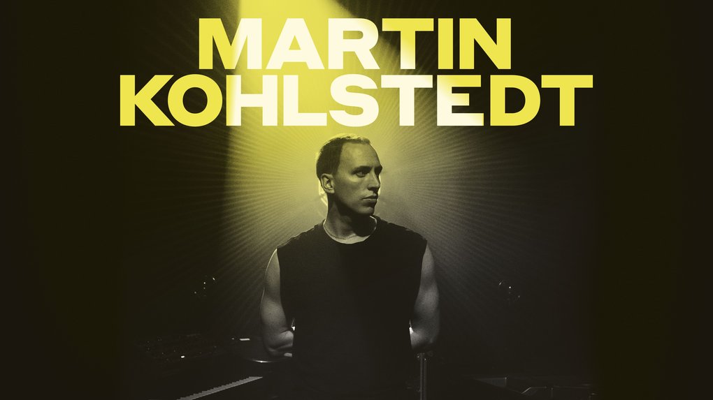 A muscular man in a black undershirt illuminated from behind by a green spotlight.