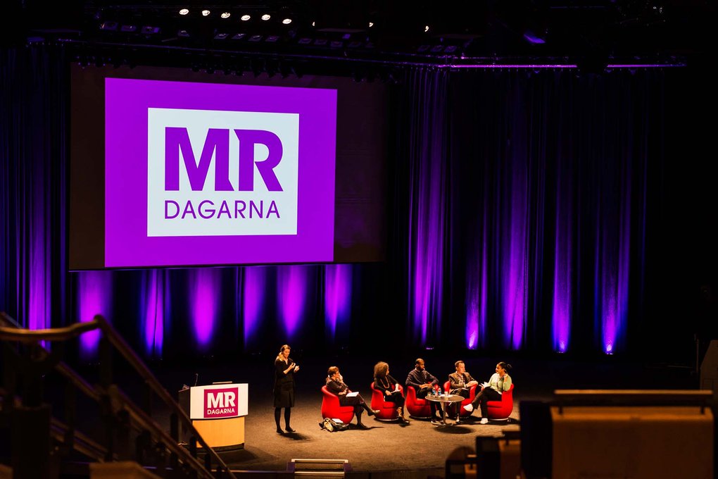 Panel på scen under MR-dagarna, stor skärm med logotyp och lila ljussättning.