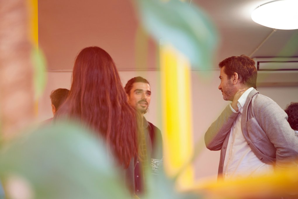 A group of people gather and chat in a relaxed setting. The image conveys the vibe of networking at an after-work event.