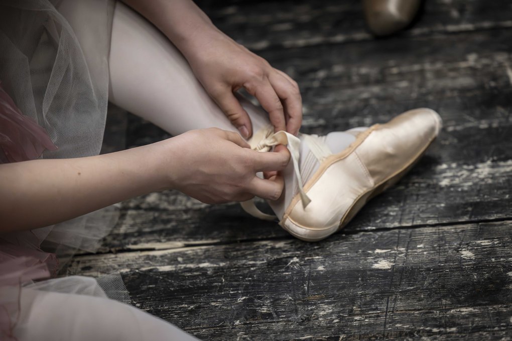 Close-up of a ballet dancer tying ribbons on a pointe shoe.