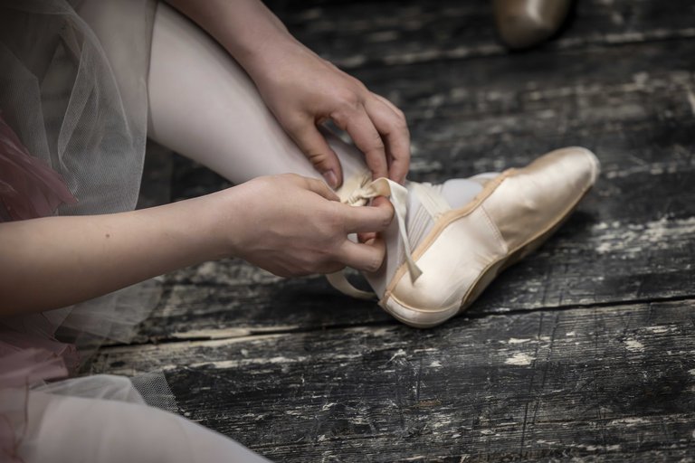 Close-up of a ballet dancer tying ribbons on a pointe shoe.