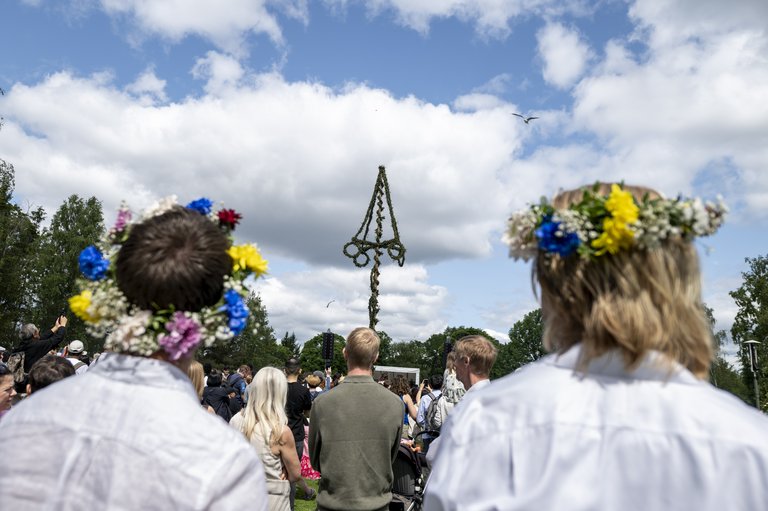 Visitors wearing flower crowns look toward the midsummer pole during Midsummer celebrations at Skansen in Stockholm.