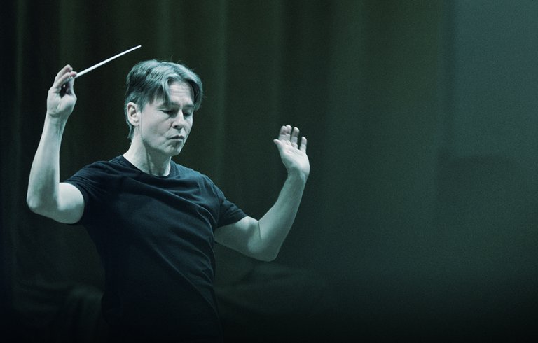 Conductor Esa-Pekka Salonen conducting against a dark green backdrop