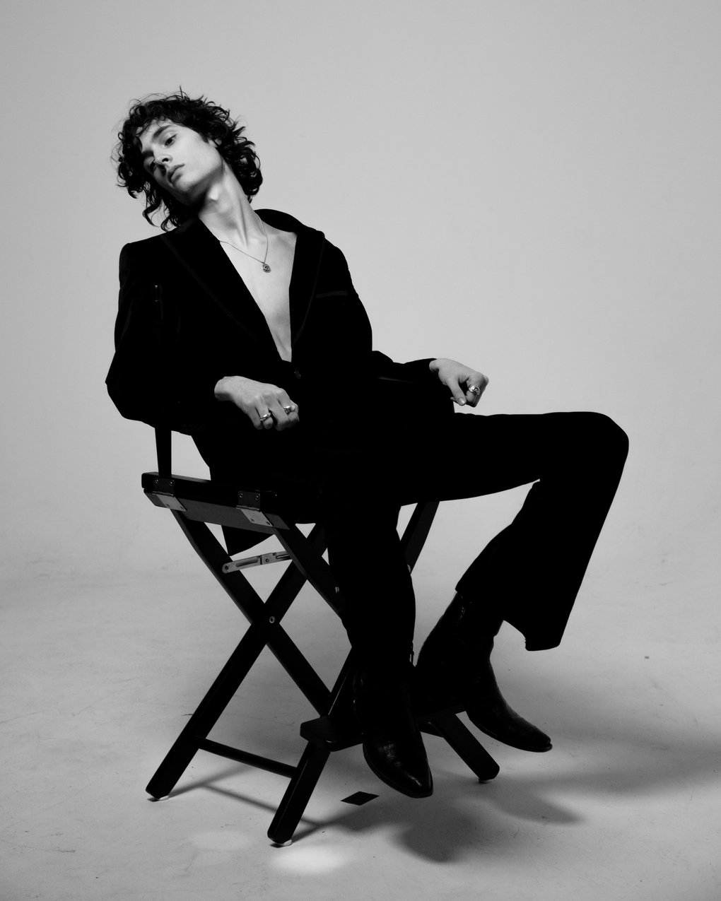 A young man in black leaning back in a Director's Chair.