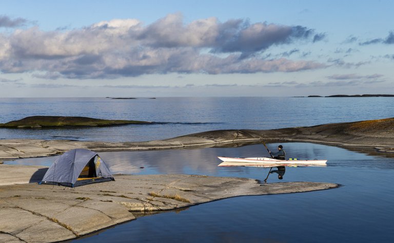 Kayaking among the cliffs in the archipelago. On one of the cliffs, you can see a small tent.