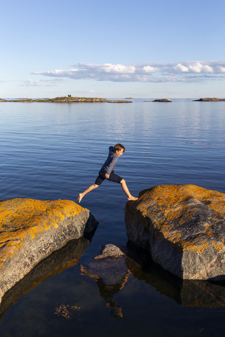 A child jumping between two small cliffs, surrounded by water.