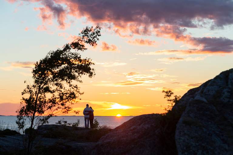 Two people, or a couple, standing closely together and looking out at the sunset.