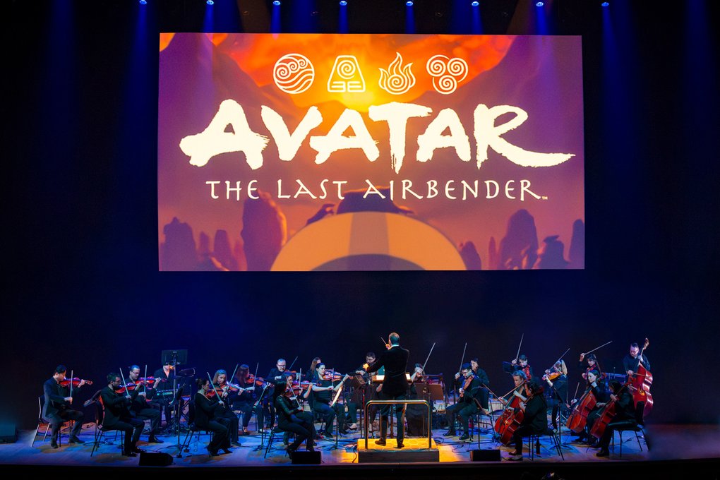 A string orchestra on a stage below a projection screen with the text: Avatar: The Last Airbender.