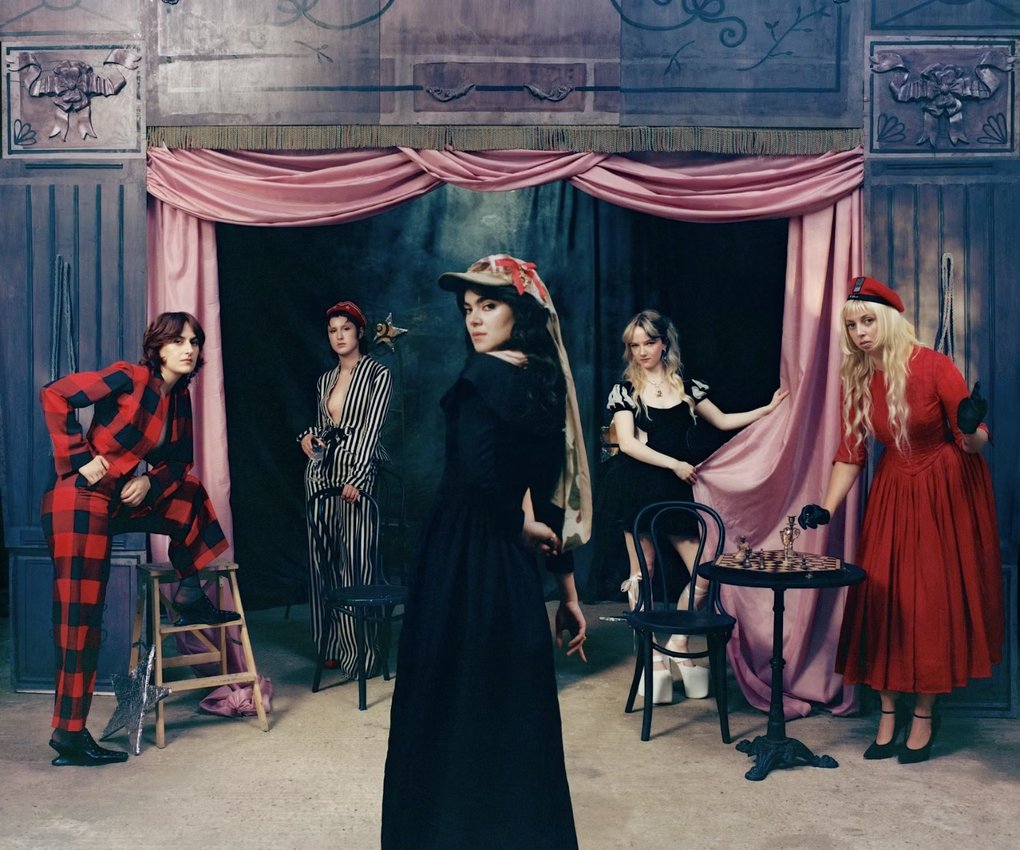 The five members of The Last Dinner Party posing in anachronistic outfits on a theater stage.