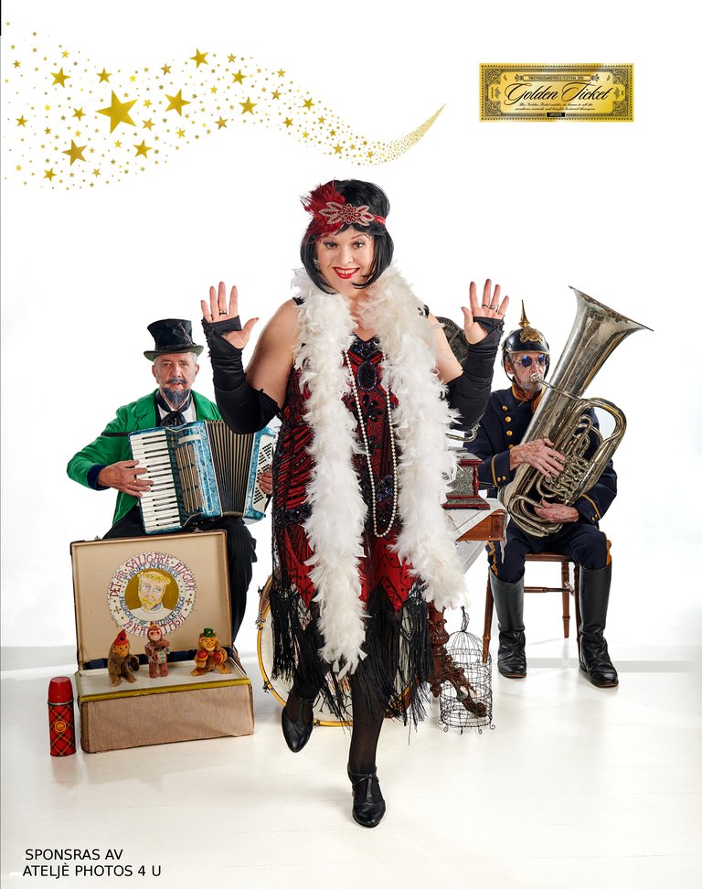 A woman in a glittery and fluffy outfit stands in front of two musicians, one playing an accordion and one playing a tuba, all posing with illuminated and festive details around them.