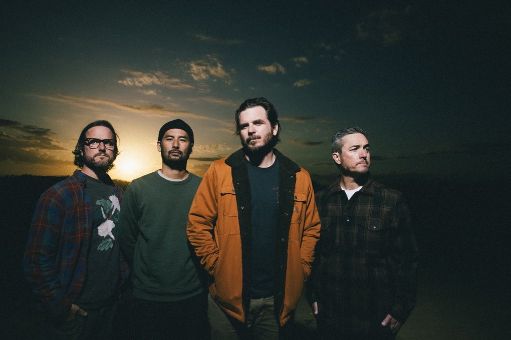 The members of Thrice standing outside, in the sunset.