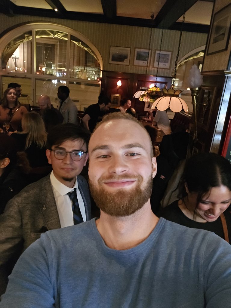 A smiling man at a social gathering in a bar, with other guests in the background