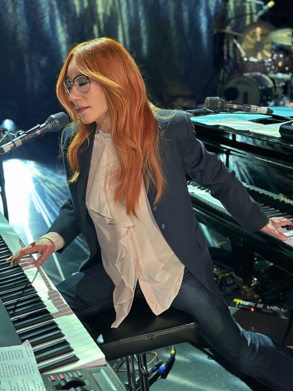 Tori Amos playing on a grand piano and a digital keyboard while singing.