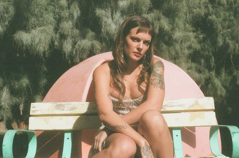 Tove Lo sitting on a bench in summer clothes.