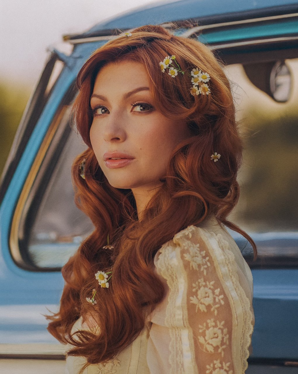 A woman with flowers in her hair, standing in front of a vintage truck.