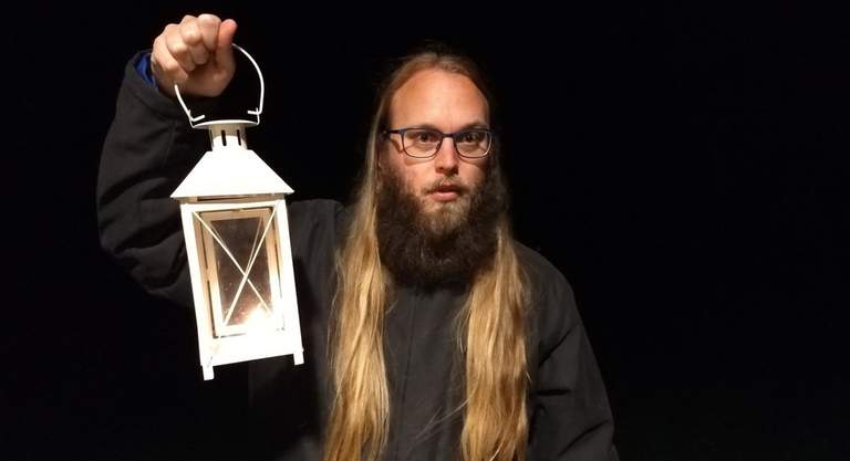 A bearded man with glasses holding a lantern